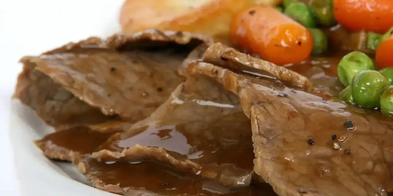 Fette di arrosto con sugo, piselli, carote e patate arrosto, un classico tra i piatti tipici del Regno Unito.