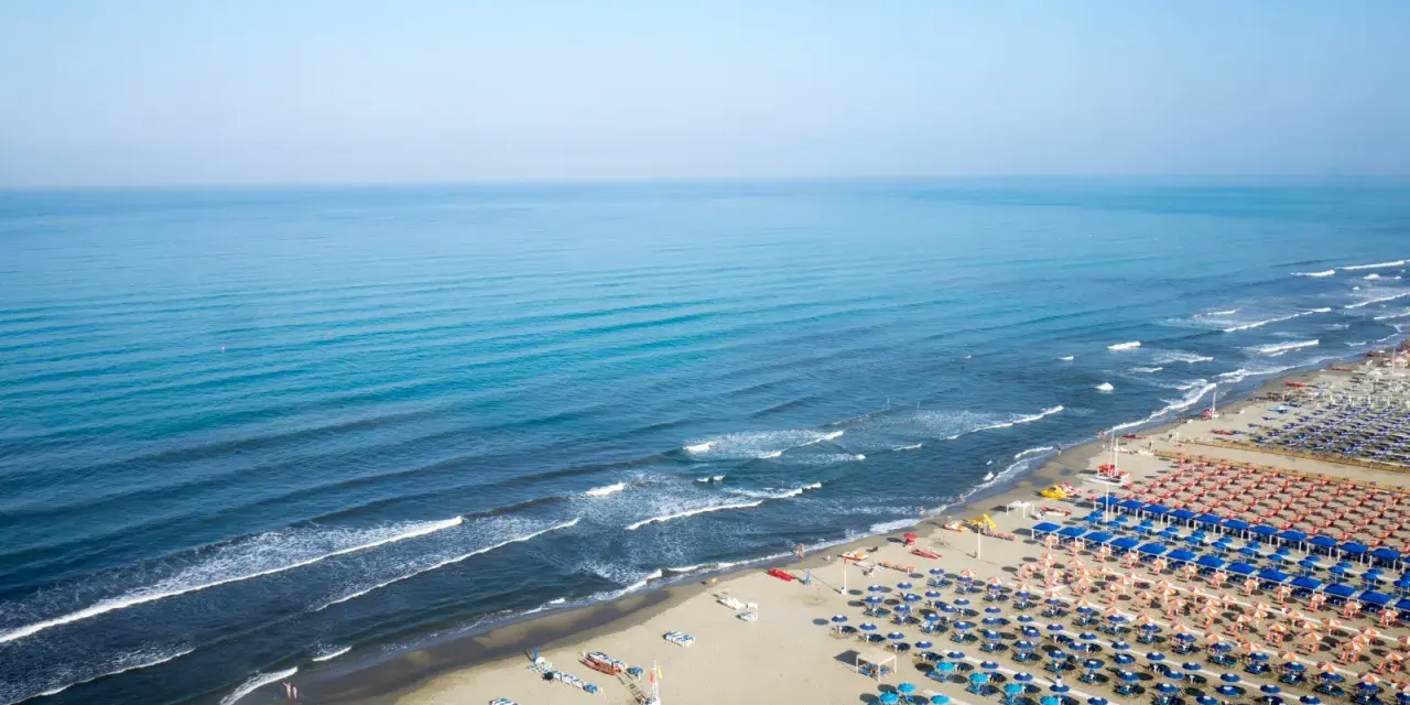 Ampia spiaggia attrezzata al lido di Camaiore, con file ordinate di ombrelloni blu e arancioni che si estendono fino al mare calmo.