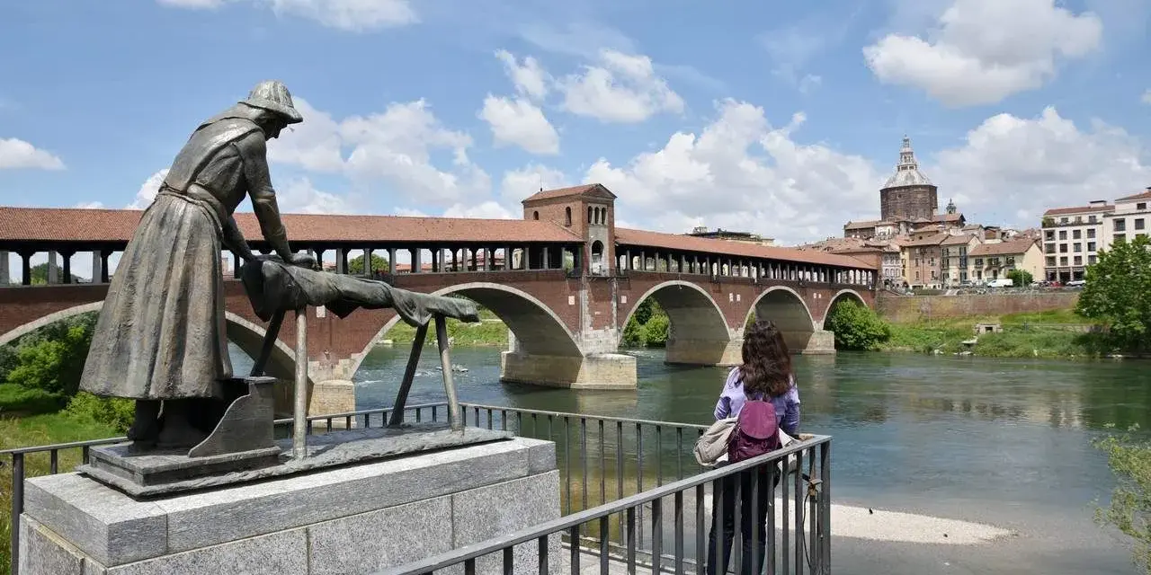 Pavia cosa vedere in un giorno: il Ponte Coperto con la statua della lavandaia e la cupola del Duomo sullo sfondo.