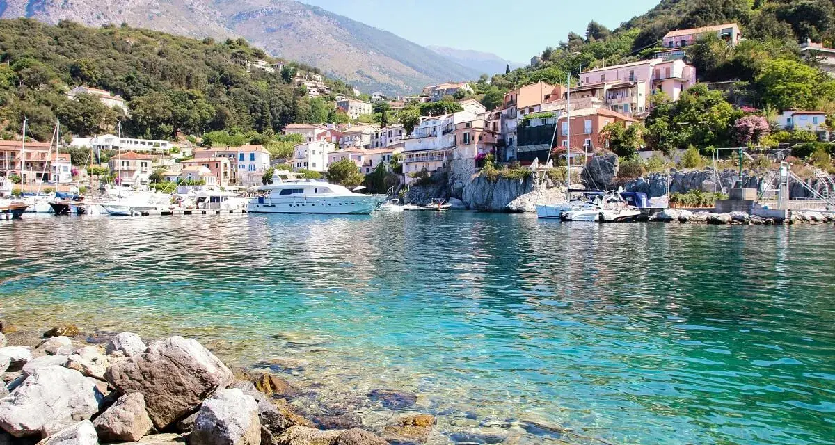 Un borgo colorato su una collina, con barche e yacht in un mare cristallino. Un esempio di posti belli da visitare in Italia a poco prezzo.