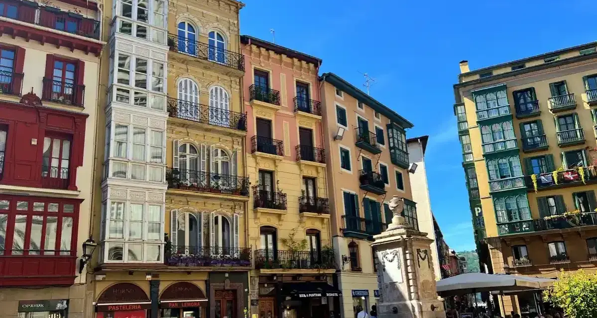 Edifici colorati con balconi in ferro battuto e una fontana in una piazza. Perfetto per scoprire cosa vedere a Bilbao in 3 giorni.