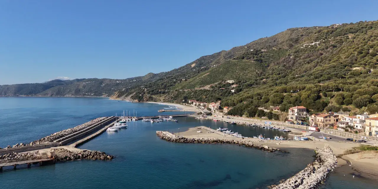 Marina di Pisciotta, con il suo porto turistico e le case aggrappate alla collina verdeggiante, sotto un cielo azzurro.