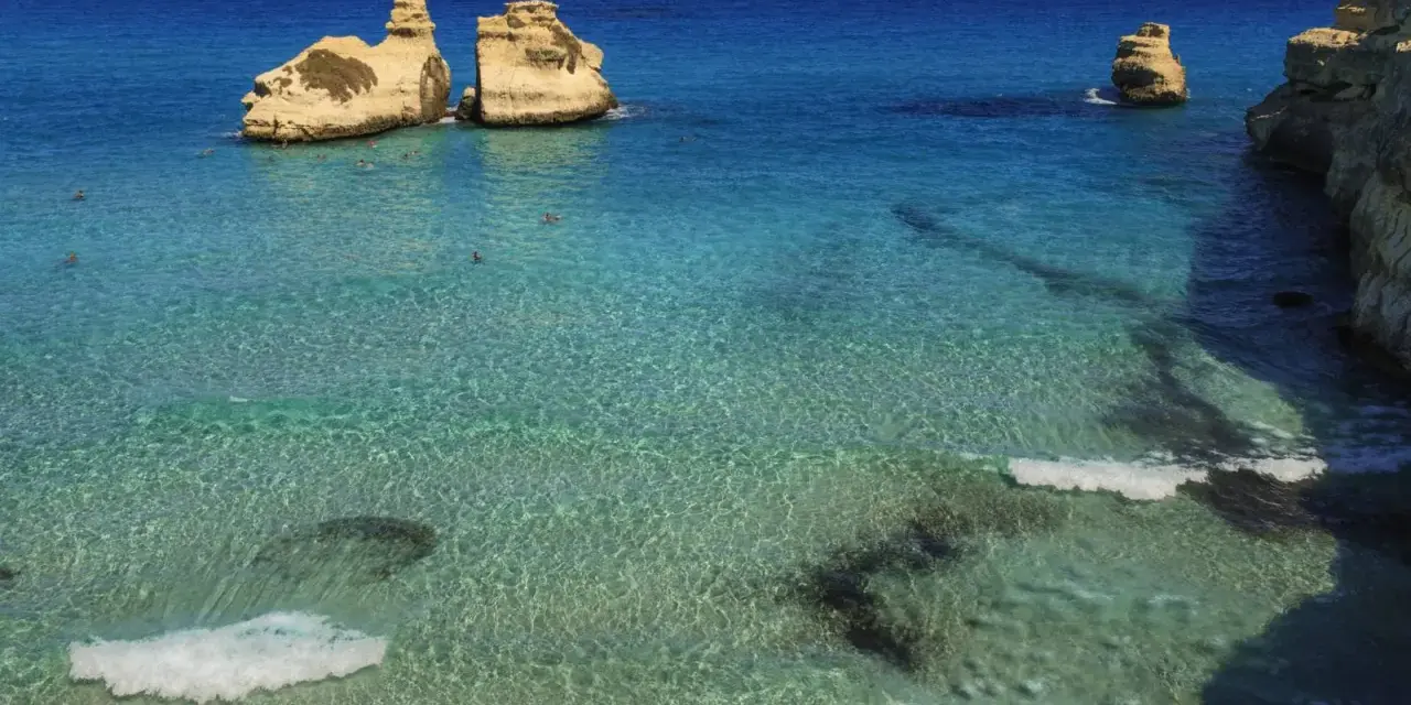 Un mare bello in Italia, con scogli dorati che emergono da acque cristalline e turchesi. Alcune persone nuotano in questo paradiso.