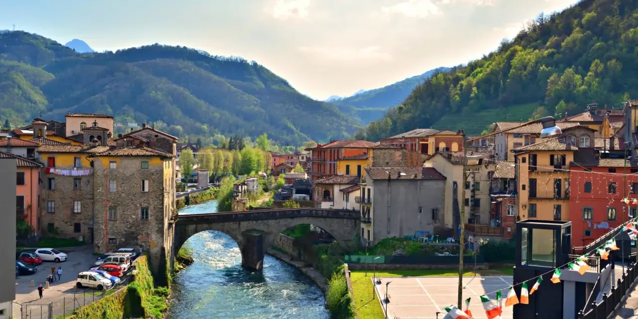 Un pittoresco scorcio di Castelnuovo di Garfagnana con il fiume Serchio che attraversa il borgo, circondato da colline verdi.