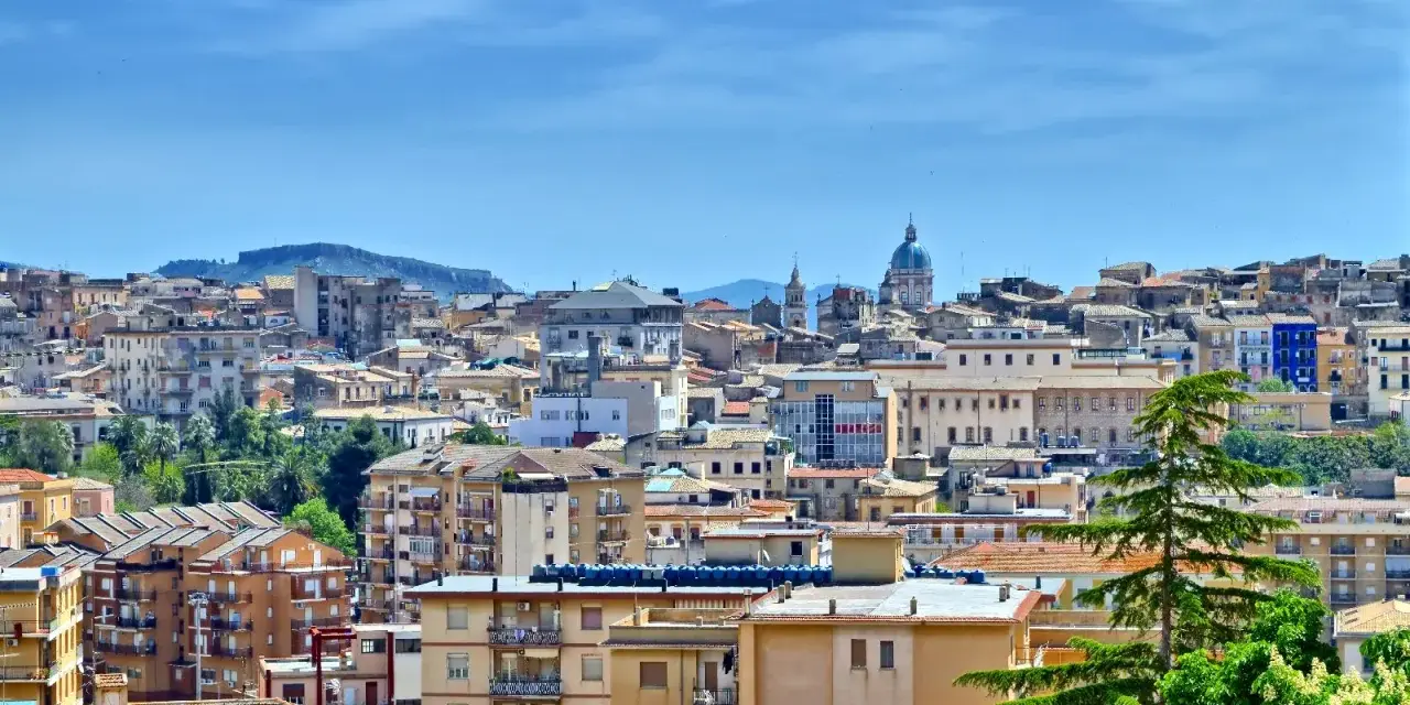 Panoramica di **Caltanissetta cosa vedere**: tetti rossi, palazzi colorati e la cupola di una chiesa sotto un cielo azzurro.
