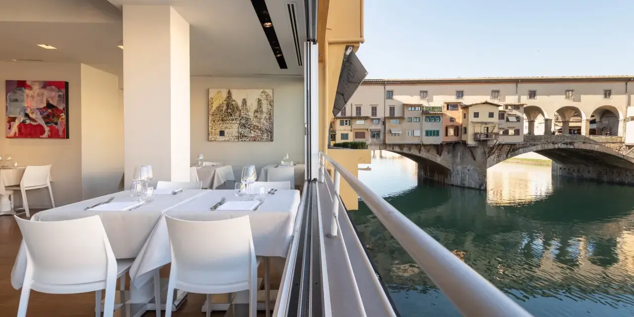 Tavoli apparecchiati in un ristorante con vista su Ponte Vecchio. Un'ottima opzione per sapere dove mangiare a Firenze.