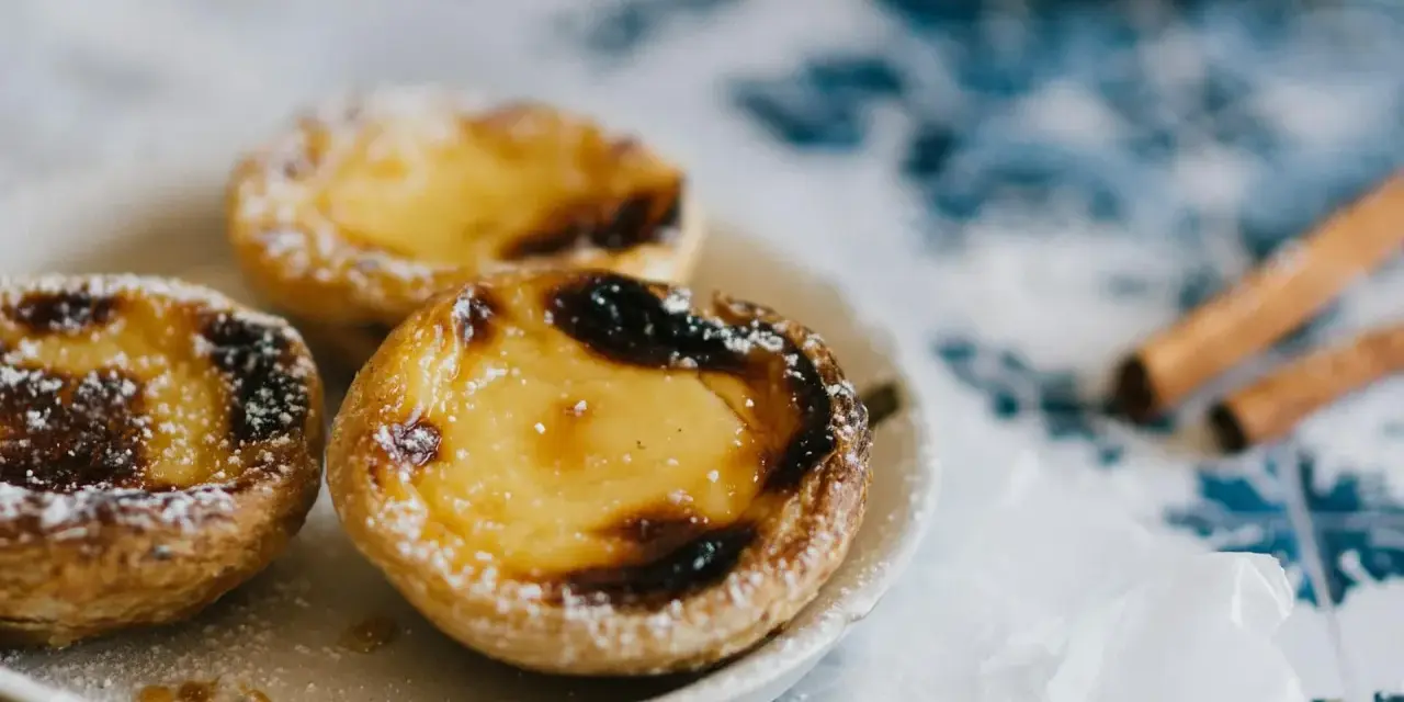 Pastéis de nata, un must per sapere cosa mangiare a Porto. Dolci cremosi su un piatto, spolverati di zucchero a velo, con cannella sullo sfondo.