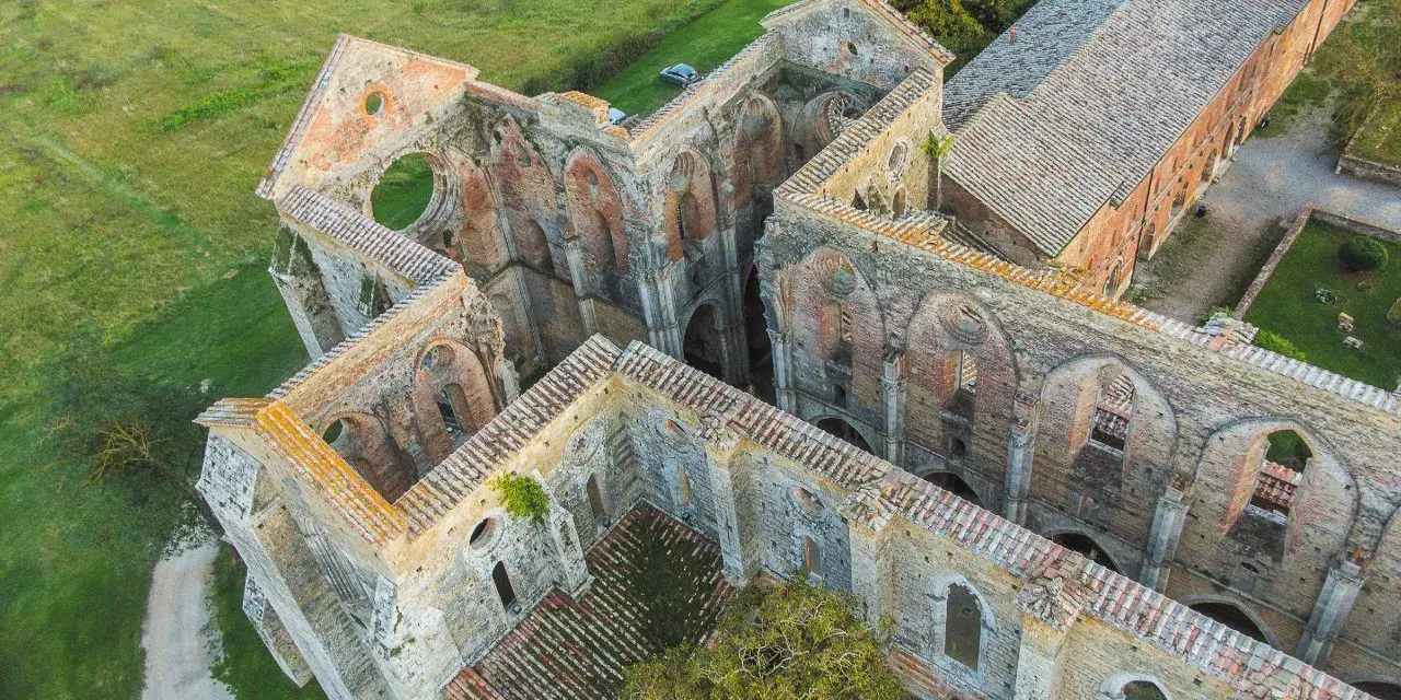 Rovine suggestive dell'abbazia nel Val di Merse, con archi gotici e tetti in tegole rosse, immerse nel verde della campagna toscana.