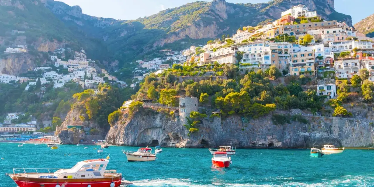 Barche a vela solcano le acque turchesi, con case colorate aggrappate alle scogliere dei paesi della costiera amalfitana.