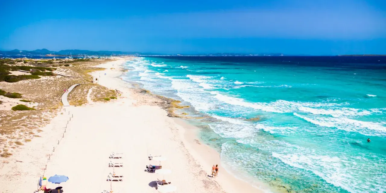 Spiaggia da sogno in Spagna dove andare al mare: sabbia bianca, acque turchesi e un sentiero tra le dune.