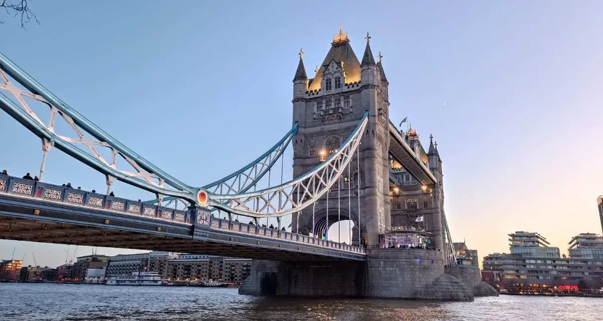 La Tower Bridge illuminata, un'icona per chi ama viaggiare a Londra, si specchia sul Tamigi al tramonto.