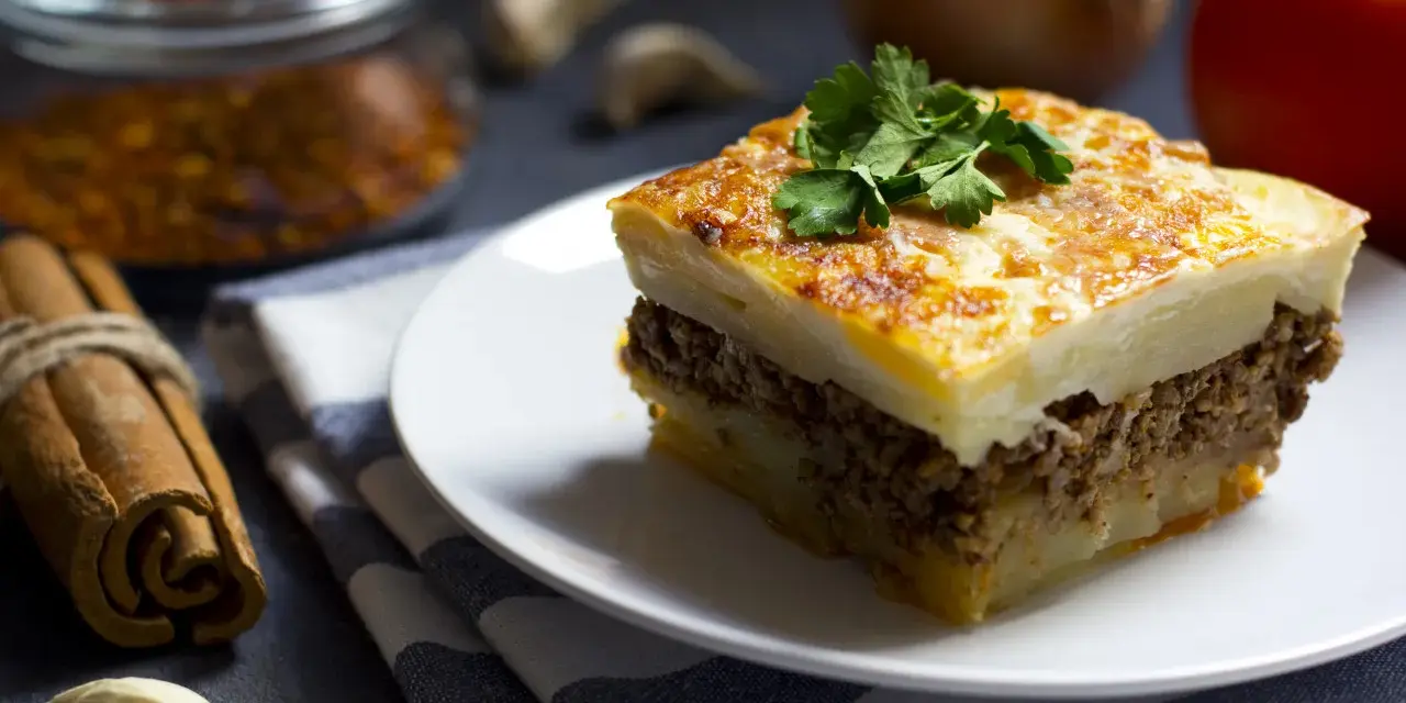 Un assaggio di cosa mangiare ad Atene: moussaka fatta in casa, con strati di patate, carne macinata e besciamella dorata, guarnita con prezzemolo fresco.