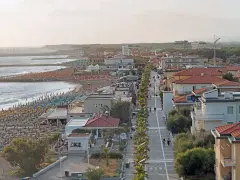 Vista aerea del lungomare di Marina di Cecina con spiaggia attrezzata, mare calmo e case con tetti rossi.