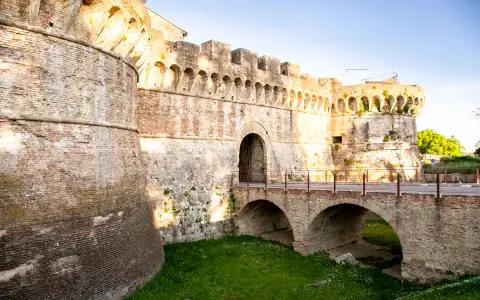 Antiche mura di Colle Val d'Elsa con un ponte ad arco che conduce a un portone fortificato.