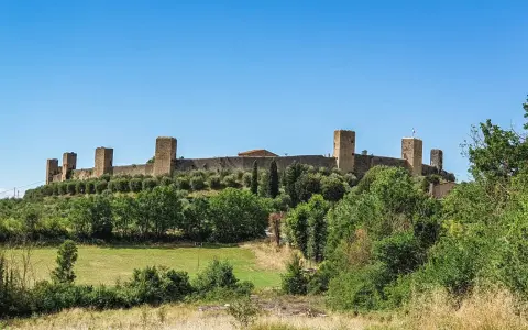 Monteriggioni cosa vedere: imponenti mura medievali con torri quadrate su una collina verdeggiante, sotto un cielo azzurro.
