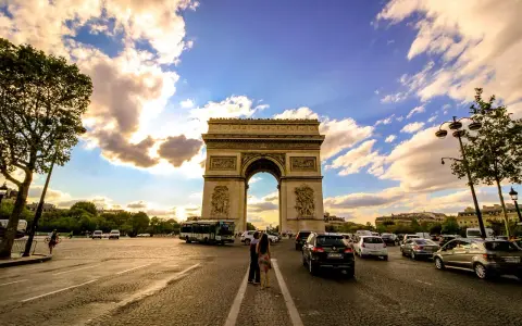 Arco di Trionfo, un'icona di cosa vedere a Parigi, con traffico e nuvole al tramonto.