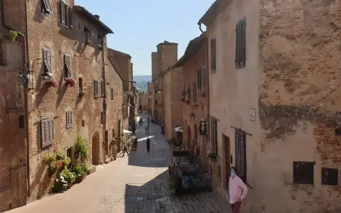 Un vicolo medievale a Certaldo, cosa vedere: case in mattoni, finestre con persiane, fiori e un uomo con mascherina.