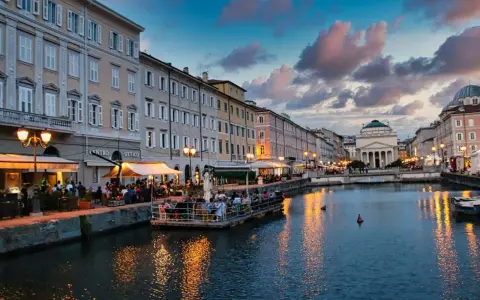 Serata magica a Trieste, uno dei tanti posti belli in Italia. Canale illuminato, palazzi storici e gente ai tavolini all'aperto.