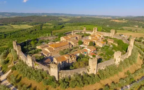 Borgo medievale fortificato nella valle del Chianti, con torri e mura antiche immerse nel verde della campagna toscana.