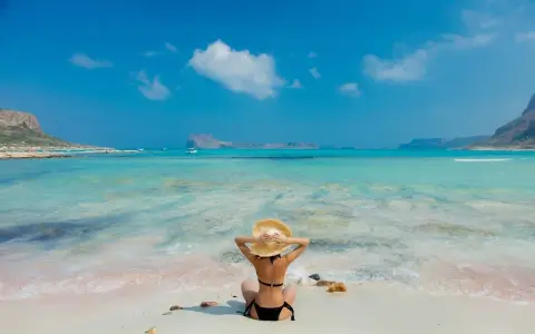 Giovane donna con cappello di paglia ammira il mare turchese, un paradiso tra le isole greche per giovani.