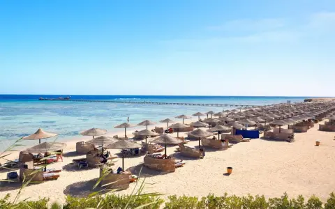 Spiaggia di Marsa Alam con file di ombrelloni e lettini, molo sull'acqua cristallina. Ideale per escursioni e relax.