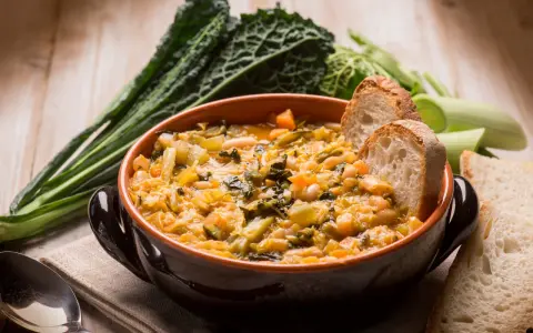 Zuppa di verdure e fagioli, un classico dei cibi tipici toscani, servita con pane rustico e contornata da cavolo nero.