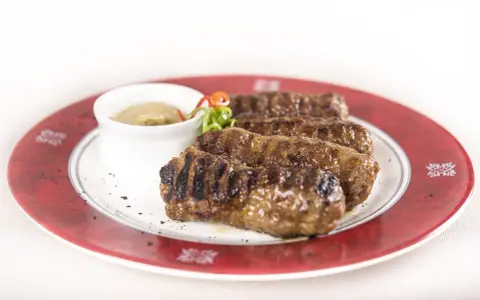 Mici grigliati su un piatto rosso, un classico per sapere cosa mangiare a Bucarest. Serviti con salsa.