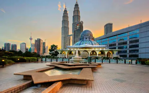 Le Petronas Towers dominano lo skyline di Kuala Lumpur, con una moschea moderna e fontane in primo piano. Un'ottima vista di cosa vedere a Kuala Lumpur al tramonto.