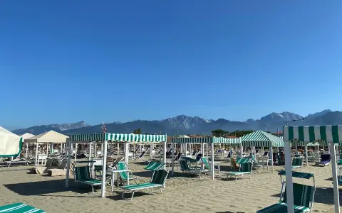 Spiaggia attrezzata a Marina di Pietrasanta con lettini e ombrelloni a righe verdi e bianche, sullo sfondo le montagne.