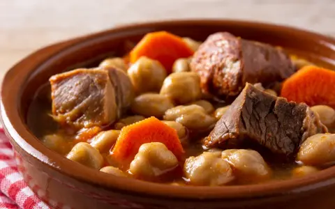 Un saporito cocido madrileño, uno dei piatti tipici di Madrid, con ceci, carne e carote in una ciotola di terracotta.