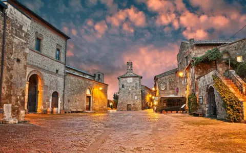 Piazza medievale illuminata al tramonto, con edifici in pietra e un campanile. Un luogo incantevole dove scoprire cosa vedere.