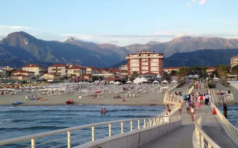 Passeggiata sul molo di Camaiore, dove si trova una spiaggia attrezzata con ombrelloni e montagne sullo sfondo.