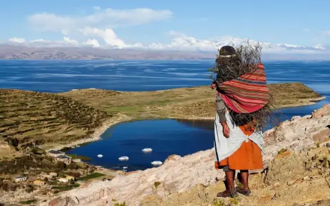Donna indigena con fascina di legna, vista sul Lago Titicaca, un luogo imperdibile da vedere in Bolivia.