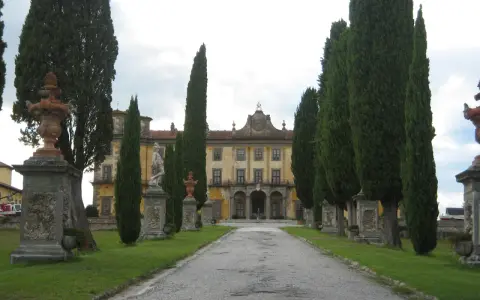 Viale alberato conduce a un palazzo giallo, con statue e fontane, tipico di un borgo a Buggiano.