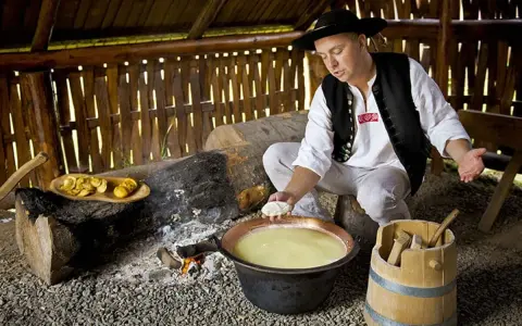 Uomo in abito tradizionale polacco prepara un prodotto tipico della Polonia: formaggio in un paiolo di rame.
