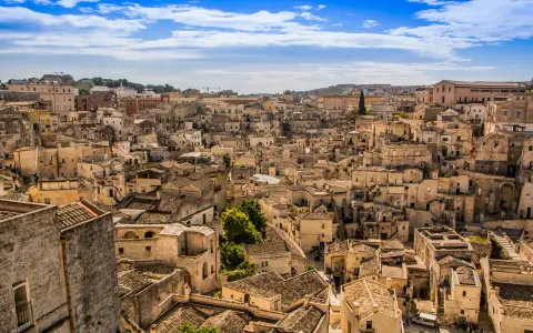 Panoramica di Matera, la città più antica del mondo, con i suoi Sassi scavati nella roccia e le case in pietra sotto un cielo azzurro.