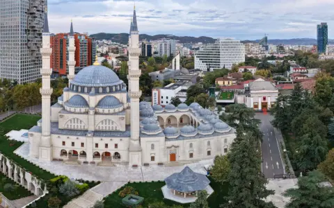 La Grande Moschea e il panorama urbano moderno mostrano dove si trova Tirana, con grattacieli e colline sullo sfondo.