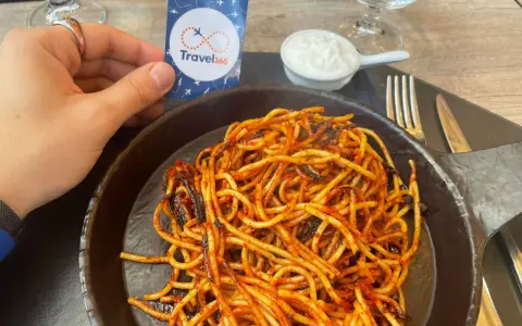 A hand holds a Travel365 tag over a plate of spaghetti with red sauce.