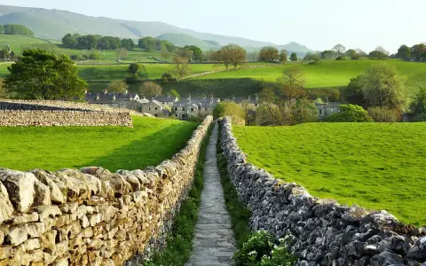 Sentiero tra muretti a secco in Yorkshire, con case di pietra e dolci colline verdi.