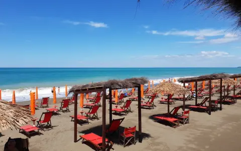 Spiaggia attrezzata a Marina di Bibbona con lettini rossi, ombrelloni di paglia e il mare azzurro sullo sfondo.