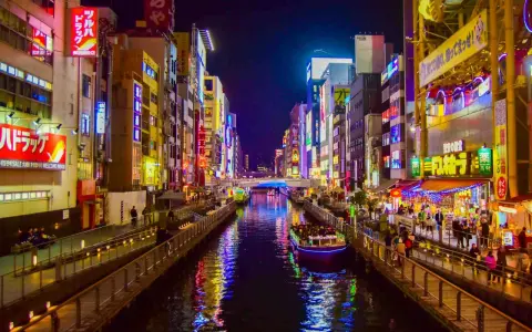 Un canale illuminato da insegne al neon a Osaka, cosa vedere: un tour in battello tra edifici vibranti e riflessi sull'acqua.