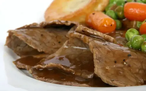 Fette di arrosto con sugo, piselli, carote e patate arrosto, un classico tra i piatti tipici del Regno Unito.