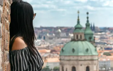 Vista di una donna con capelli scuri appoggiata a un muro di mattoni, con lo sguardo rivolto verso un panorama urbano di **città europee da visitare in 3 giorni**.