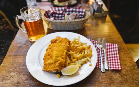 Piatto di pesce fritto e patatine fritte, con una birra chiara, un classico per scoprire cosa mangiare a Lubiana.