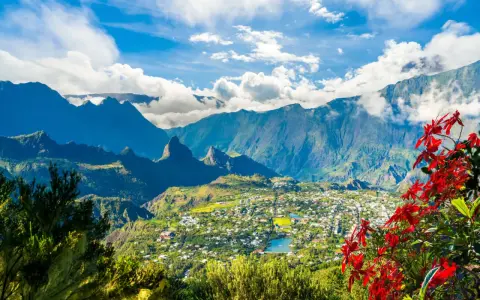 Vista panoramica di un villaggio verdeggiante sull'isola di Reunion, incastonato tra imponenti montagne blu e fiori rossi vibranti.