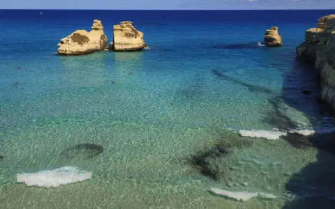 Un mare bello in Italia, con scogli dorati che emergono da acque cristalline e turchesi. Alcune persone nuotano in questo paradiso.