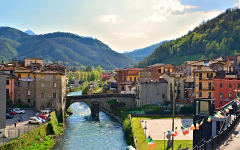 Un pittoresco scorcio di Castelnuovo di Garfagnana con il fiume Serchio che attraversa il borgo, circondato da colline verdi.