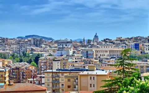 Panoramica di **Caltanissetta cosa vedere**: tetti rossi, palazzi colorati e la cupola di una chiesa sotto un cielo azzurro.