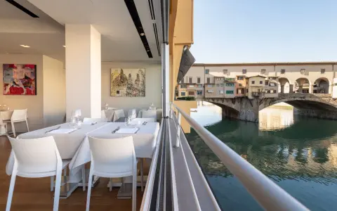 Tavoli apparecchiati in un ristorante con vista su Ponte Vecchio. Un'ottima opzione per sapere dove mangiare a Firenze.