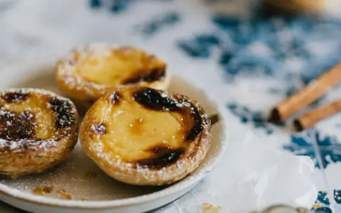Pastéis de nata, un must per sapere cosa mangiare a Porto. Dolci cremosi su un piatto, spolverati di zucchero a velo, con cannella sullo sfondo.